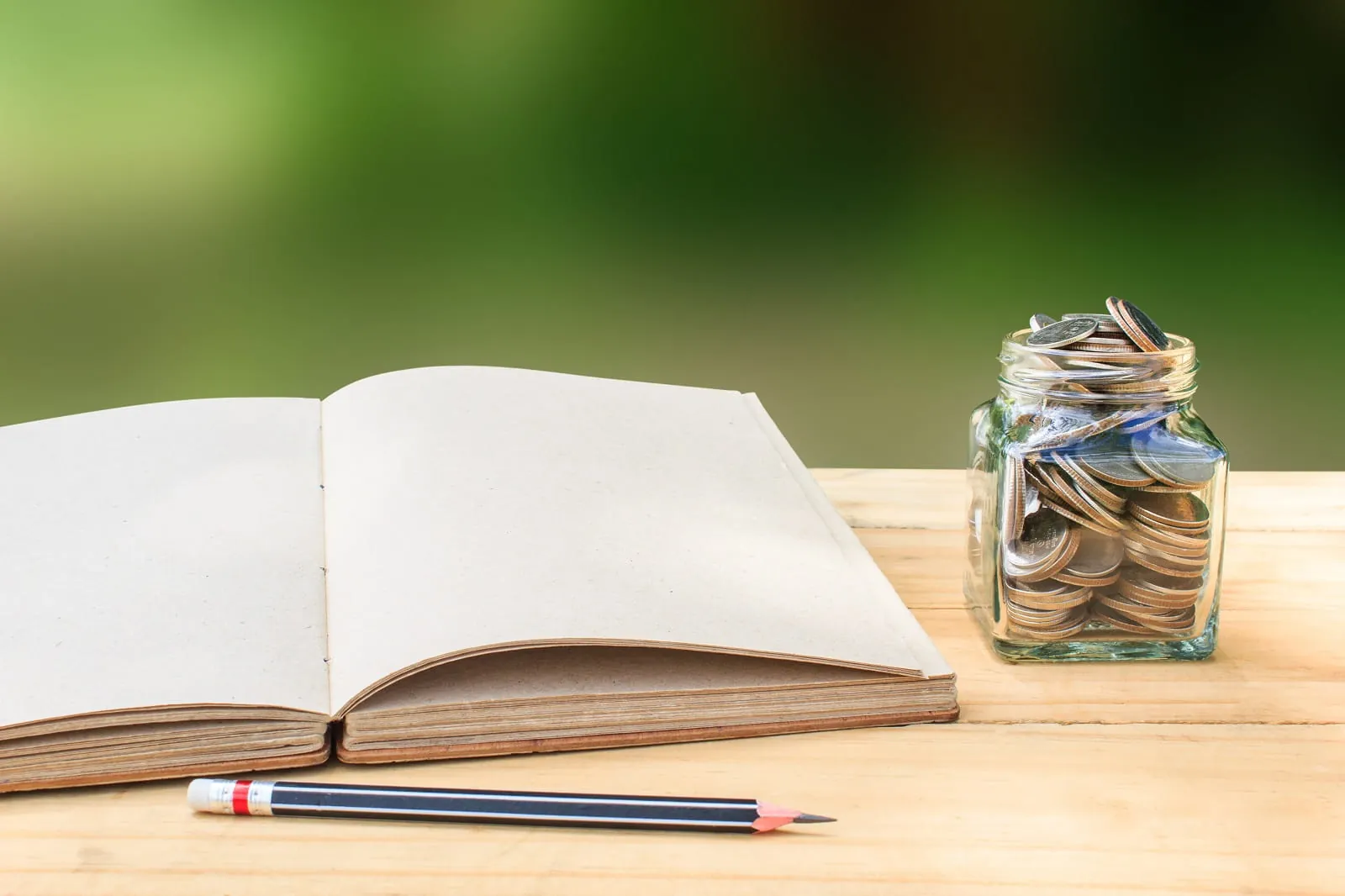 Open notebook, pencil and a jar of coins on a wooden table