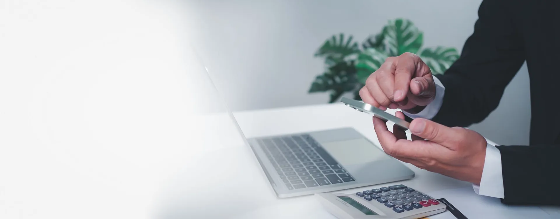 Professional using a phone and calculator beside a laptop