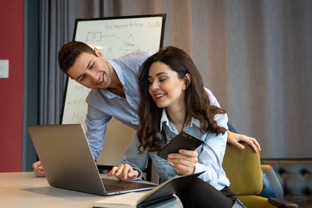 Two colleagues smiling while working on a laptop in an office