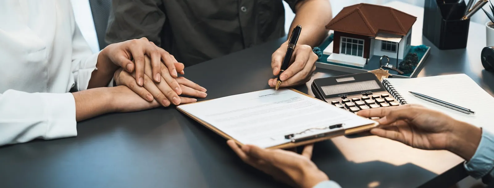 Signing a loan document beside a calculator and a model house