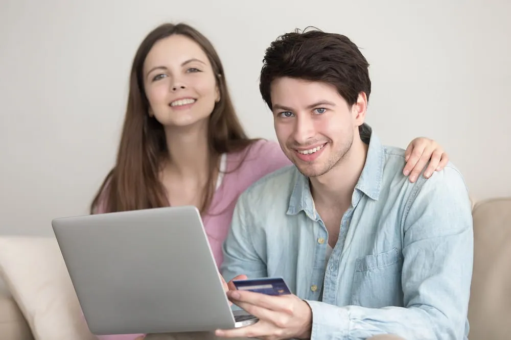 Smiling couple with a laptop and a card on a sofa