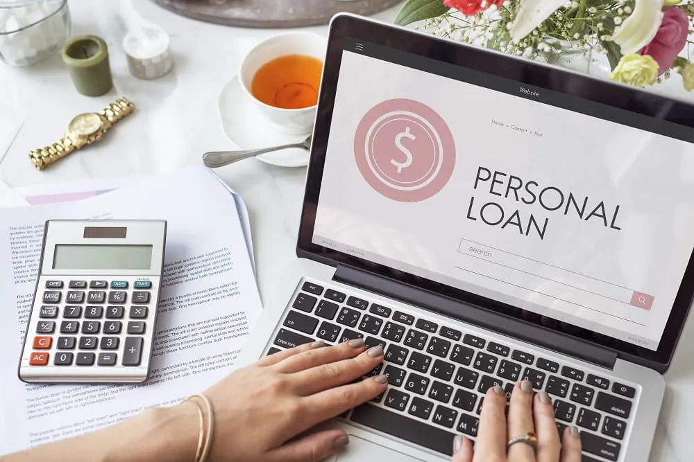 Hands typing on a laptop showing a personal loan page beside a calculator