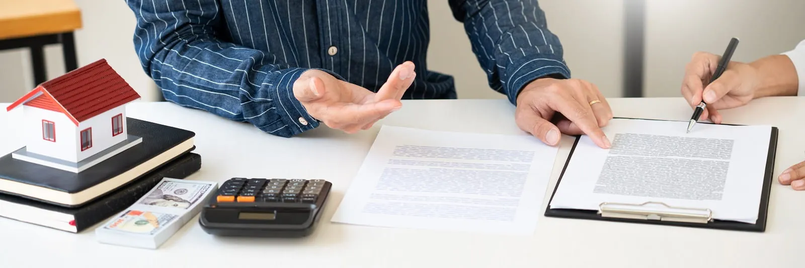 Advisor and client going over loan papers beside a calculator and a model house